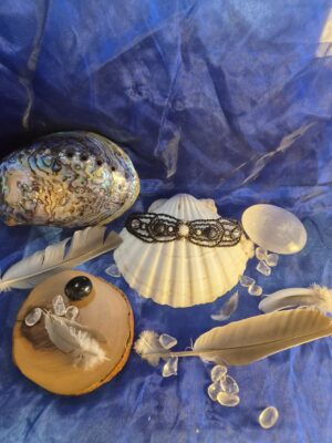 Bracelet talisman Le Pilier Silencieux présenté dans un univers alchimique avec coquillage, plumes et cristaux.